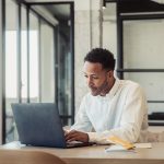 Eine Person in einem Büro sitzt vor einem Laptop und tippt auf der Tastatur.