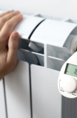 Smarte Thermostate, So kannst du deine Heizung fernsteuern Eine Person fasst an eine Heizung, an der ein elektronisches Thermostat sitzt.