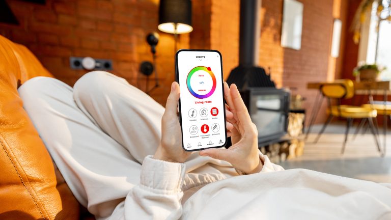 Eine Person hält ein Smartphone in der Hand, auf der die App-Steuerung von smarter Beleuchtung zu sehen ist.