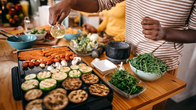 Grill und Grillrost sauber machen: Die besten Tipps und Hausmittel Eine Person gießt etwas Öl über das Grillgut auf einem Elektrogrill.
