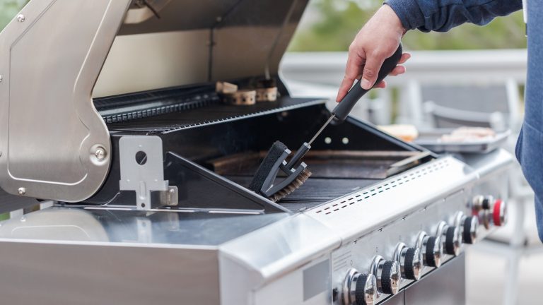 Grill und Grillrost sauber machen: Die besten Tipps und Hausmittel Eine Person bürstet mit einer Grillbürste verbrannte Reste von einem Grillrost.