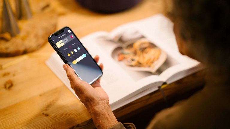 Eine Person hält ein Smartphone in der Hand, auf der die Lichtsteuerung smarter Beleuchtung zu sehen ist.