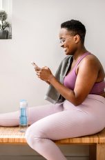Eine Person sitzt in Sportoutfit zu Hause und scrollt auf ihrem Smartphone.