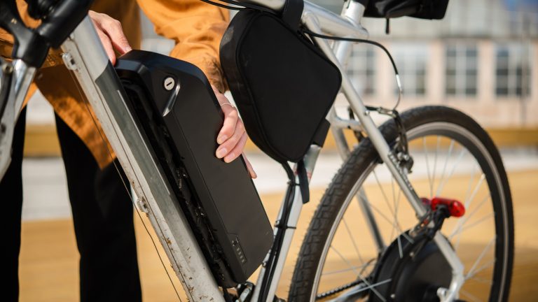 Eine Person hat die Hände an dem Akku ihres E-Bikes.