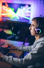 Eine Person sitzt vor einem Gaming Set-up mit bunten LED-Lichtern im Hintergrund.