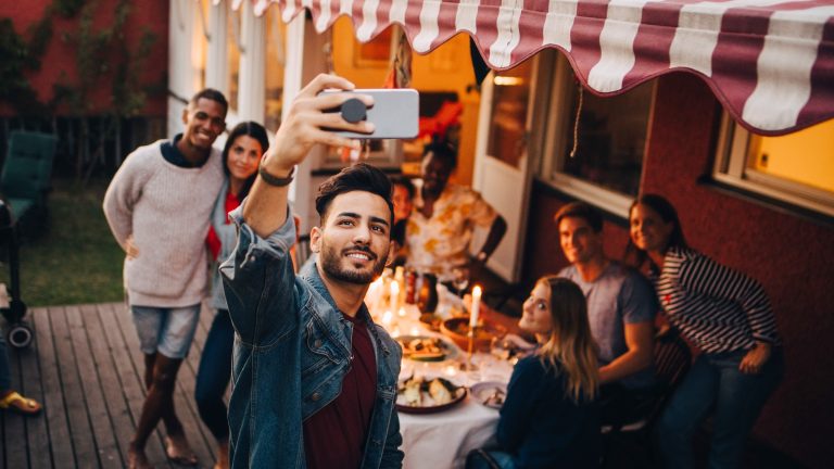 Eine Gruppe an Personen hat sich auf einer Terrasse unter einer gestreiften Markise versammelt.