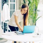 Eine Person bückt sich zu einem Laptop auf einem Tisch herunter und tippt etwas darauf.