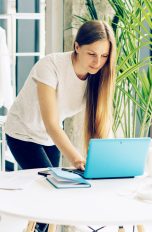 Eine Person bückt sich zu einem Laptop auf einem Tisch herunter und tippt etwas darauf.