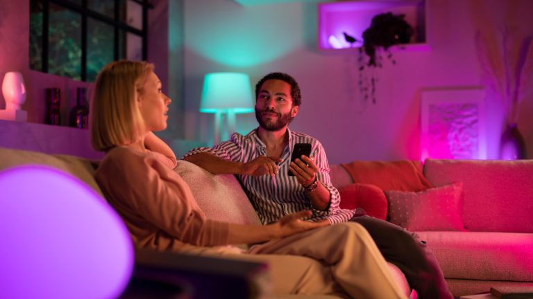 Zwei Personen sitzen in einem bunt beleuchteten Raum auf einem Sofa.