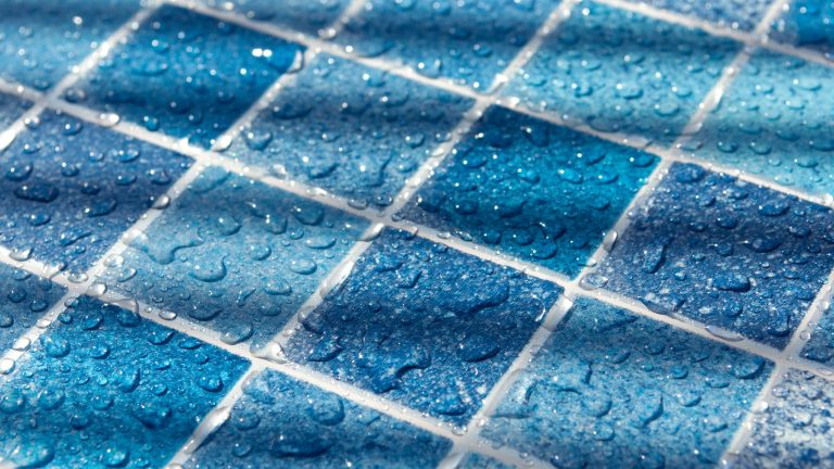 Fliesenfugen ausbessern Blick auf einen blauen Fliesenboden, auf dem Wassertropfen zu sehen sind.