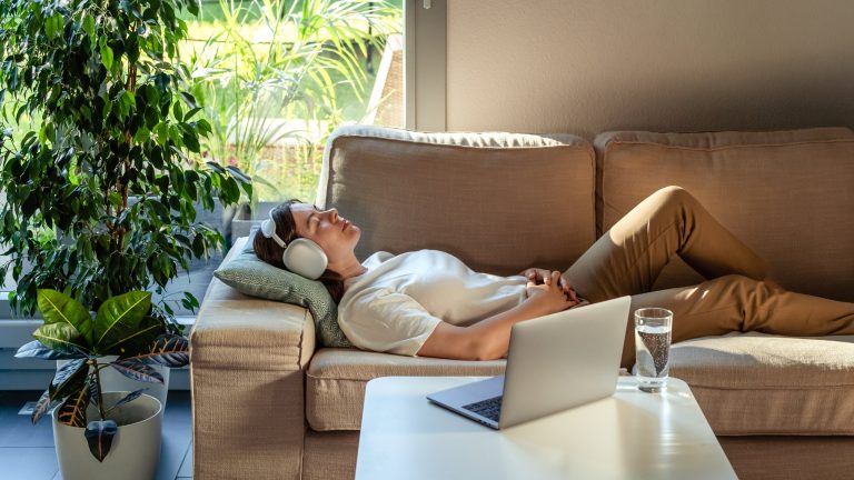 Spotify, So nutzt du es unter iOS und Android Eine Person liegt auf einem Sofa und hört über Kopfhörer Musik von einem verbundenen Laptop.