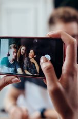 Fotos versenden auf WhatsApp Eine Person macht mit dem Smartphone ein Foto von drei anderen Personen.