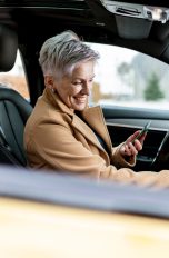 Eine Person sitzt in einem Auto und tippt auf dem Infotainment-System des Autos herum. In der anderen Hand hält sie ein Smartphone.