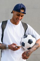 Eine Person mit einem Fußball unter dem Arm schaut auf ihr Smartphone.