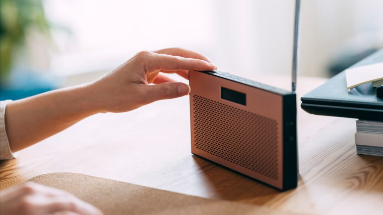 Radioempfang verbessern Eine Person drückt einen Knopf an der Oberseite eines schmalen, kleinen Radios auf einem Schreibtisch.