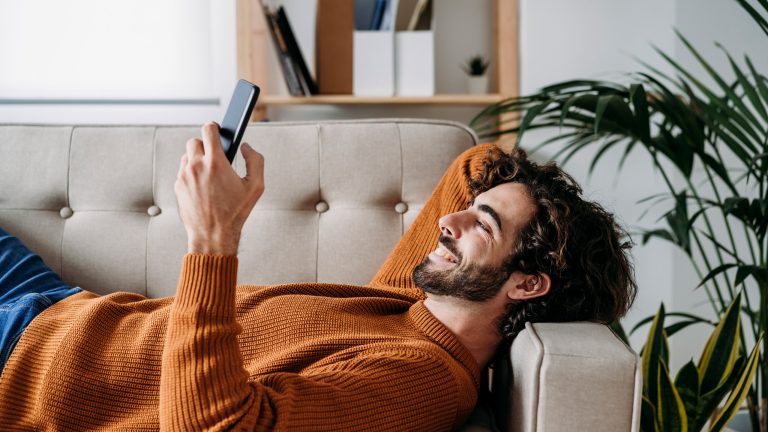 TikTok Coins, so lädst du sie auf und verteilst Geschenke Eine Person liegt in einem Wohnzimmer auf der Couch und scrollt auf ihrem Smartphone.