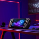 Ein ROG Ally X steht auf einer Halterung auf einem Schreibtisch, auf dem ein ROG-Gaming-Monitor zu sehen ist.