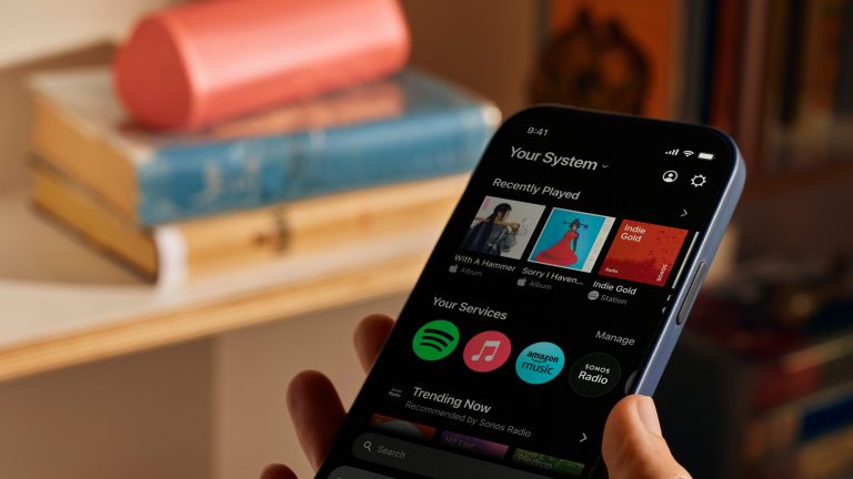 Spotify auf Sonos, Sonos App Blick auf ein Smartphone mit geöffneter Sonos-App. Im Hintergrund ist ein Lautsprecher zu sehen.