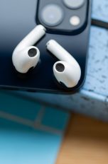Zwei AirPods liegen auf der Rückseite von einem iPhone.