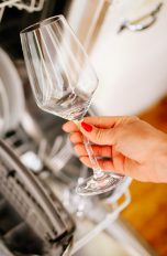 Eine Person hält ein Glas in der Hand, das sie anscheinend aus der Spülmaschine im Hintergrund genommen hat.