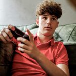 Eine Person mit einem Controller in der Hand sitzt vor einem Sofa.