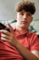 Eine Person mit einem Controller in der Hand sitzt vor einem Sofa.