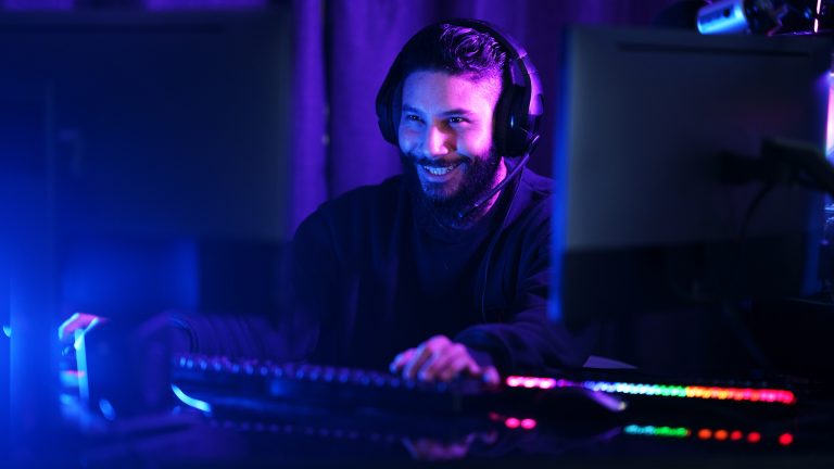 Twitch und Prime, Account verbinden und kostenlos subscriben Eine Person mit Headset auf dem Kopf sitzt vor einem bunt leuchtenden Gaming-Setup.