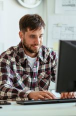 Eine Person sitzt lächelnd in einem Büro vor einem Rechner.