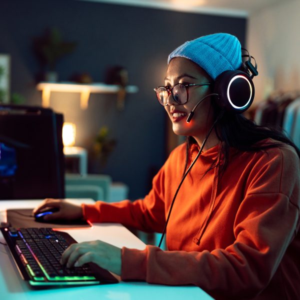 Eine Person mit Headset auf dem Kopf sitzt an einem Schreibstisch vor zwei Monitoren neben einem Gaming-PC.