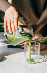Eine Person gießt zerkleinertes Obst und Gemüse von einem Zerkleinerer in ein Glas.