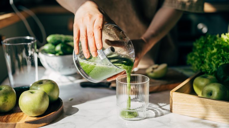 Eine Person gießt zerkleinertes Obst und Gemüse von einem Zerkleinerer in ein Glas.