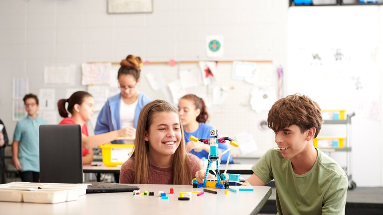 LEGO Spike, Nachfolger von Mindstorms im Überblick Zwei Kinder bauen einen Roboter mit LEGO Spike. Im Hintergrund sind weitere Kinder zu sehen.