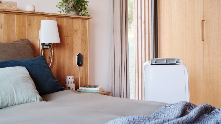 Smarte Klimaanlagen, Temperatur per Handy steuern Ein kleines freistehendes Klimagerät steht in einem Schlafzimmer neben einem Bett.