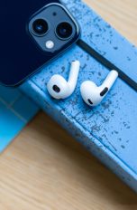 Zwei AirPods liegen neben einem iPhone auf einem Notizbuch.