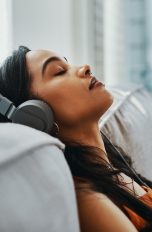Eine Person sitzt auf einem Sofa, lehnt sich zurück und hört über Kopfhörer Musik.