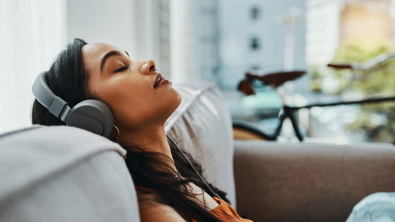 Eine Person sitzt auf einem Sofa, lehnt sich zurück und hört über Kopfhörer Musik.