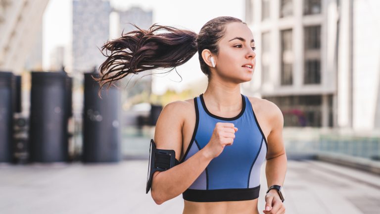 iCloud-Musikmediathek, Aktivieren, nutzen und deaktivieren Eine Person mit einem Smartphone am Arm und Kopfhörern im Ohr treibt draußen Sport.