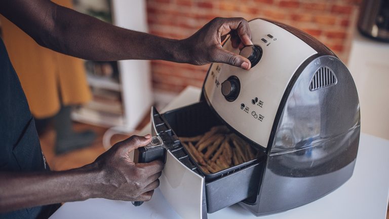 Airfryer - welche gibts. Philips, tefal, ninja Ein Mensch öffnet die Schublade eines Airfryers in dem Frittiertes zu sehen ist.