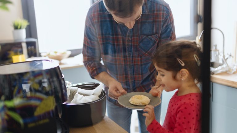 Airfryer - welche gibts. Philips, tefal, ninja Eine Person steht mit einem Kind vor einem geöffneten Airfryer und begutachtet einen Donut auf einem Teller.