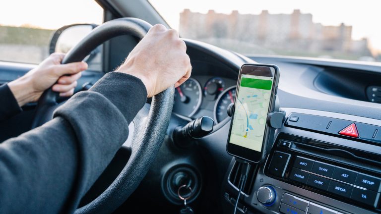 Android Auto funktioniert nicht, Wenn die Verbindung hakt Eine Person fährt Auto. Am Lüftungsgitter ist ein Smartphone mit aktivierter Navigation angebracht.