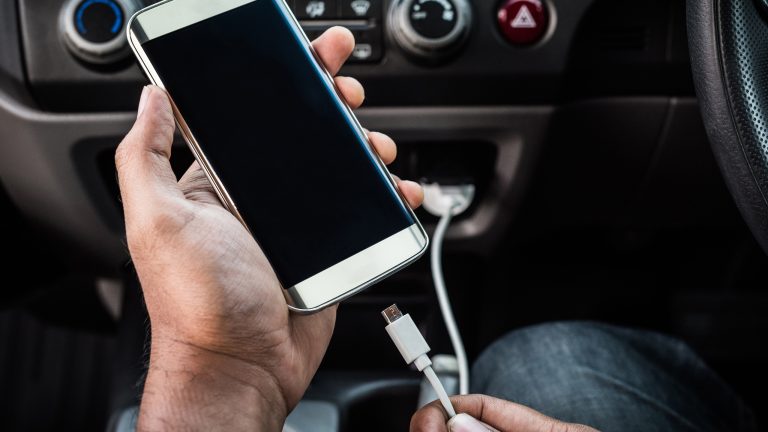 Android Auto funktioniert nicht, Wenn die Verbindung hakt Eine Person steckt ein Smartphone an ein Kabel an, das ans Auto angeschlossen ist.
