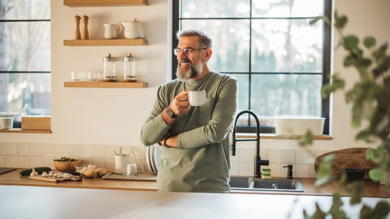 Dolce Gusto entkalken und reinigen, So geht’s Eine Person steht mit einer Kaffeetasse angelehnt an der Küchentheke.