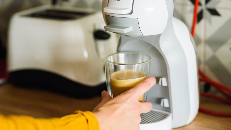 Dolce Gusto entkalken und reinigen, So geht’s Eine Person nimmt einen frischen Kaffeebecher vom Becherhalter einer Dolce Gusto Maschine.