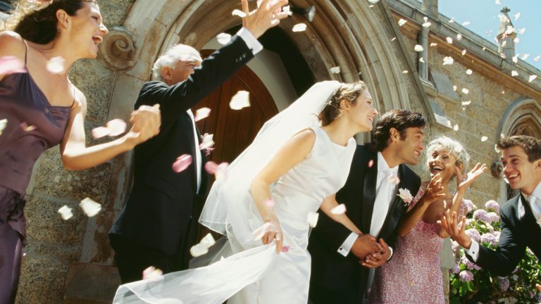 Ein Hochzeitspaar kommt aus einer Kirch. Die Hochzeitsgemeinschaft wirft Blüten in die Luft.