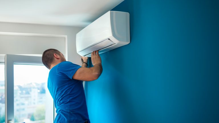 Klimaanlage, Diese Typen gibt es, dann lohnt sie sich Eine Person kontrolliert eine offenbar frisch angebrachte Split-Klimaanlage, die an einer Wand hängt.