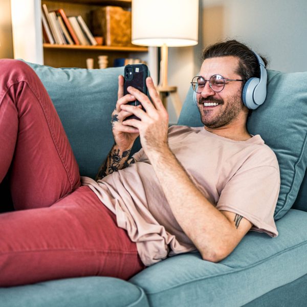 Eine Person liegt auf einem Sofa, trägt Kopfhörer und hält ein Smartphone in der Hand.