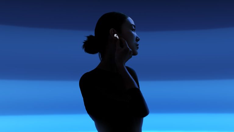 AirPods 2024, Die neue Audio-Generation Eine Person im Dunkeln vor neon leuchtendem Hintergrund mit einem AirPod im Ohr.