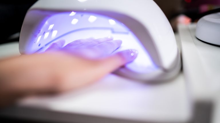 UV-Manikuere zuhause, Alternativen zu Neonail Eine Person hält eine Hand unter eine UV-Lampe zum Aushärten des Nagellacks.