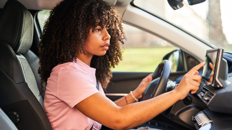 Apps für Android Auto, Praktische Programme für die Fahrt Eine Person sitzt ein einem Auto und bedient das Display von ihrem Infotainmentsystem.