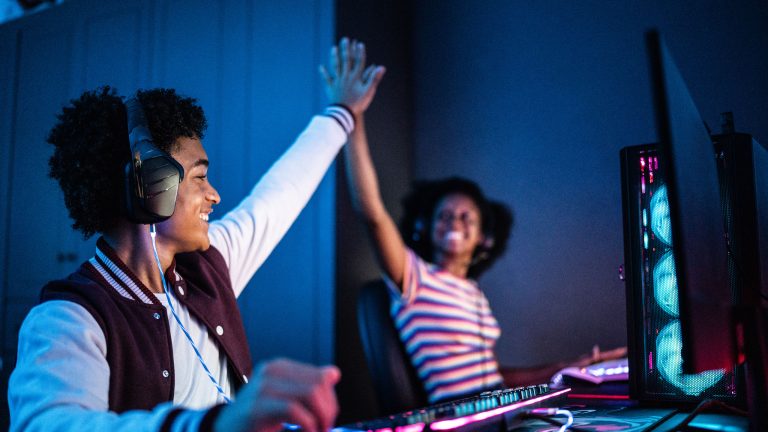 Soundboards bei Discord verwenden, Der ultimative Ratgeber Zwei Personen sitzen nebeneinander an Gaming-PCs und geben sich ein High Five.
